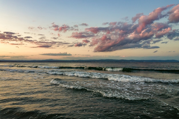 Superfície do mar com as ondas de água azul sob o céu amarelo e roxo por do sol.