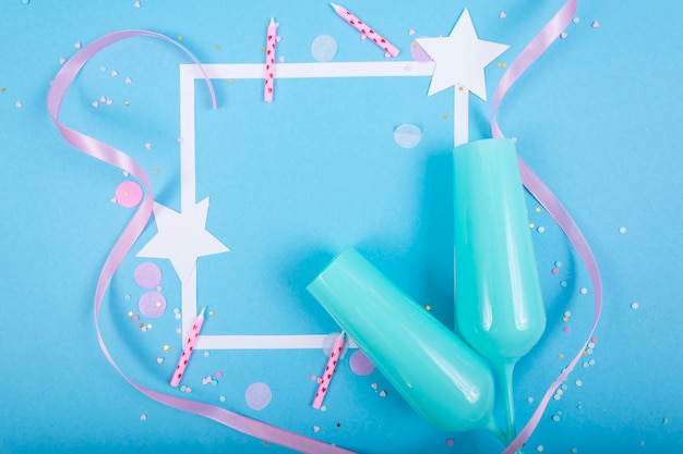 Superficie de fiesta con cinta, estrellas, velas de cumpleaños, marco vacío de caja de regalo y confeti sobre superficie azul