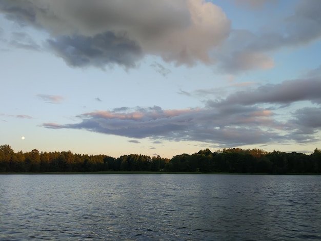 Superficie del lago en calma al atardecer en Letonia, Europa del Este. paisaje de puesta de sol de verano con agua y bosque.