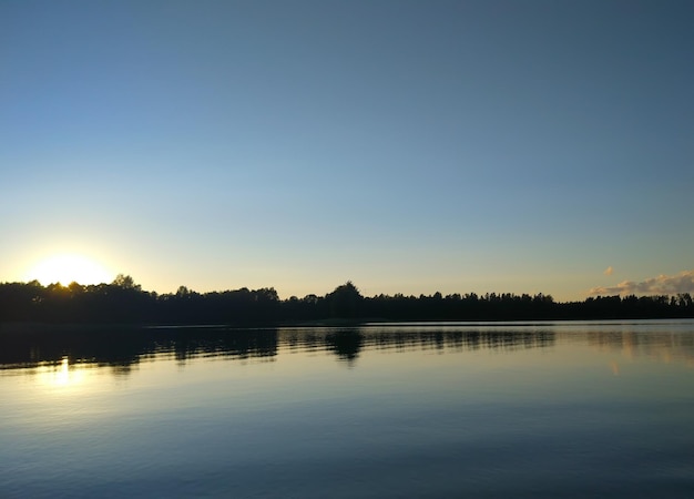 Superficie del lago en calma al atardecer en Letonia, Europa del Este. paisaje de puesta de sol de verano con agua y bosque.
