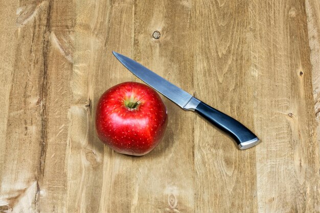 En la superficie de madera hay una manzana roja y un cuchillo