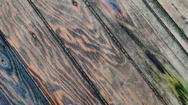 Superficie de madera hecha de tablas con manchas multicolores de líneas diagonales de humedad vista superior de cerca