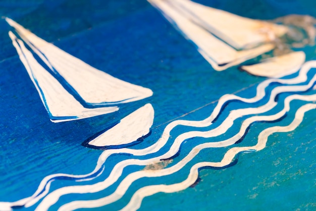 Superficie de madera pintada de azul y blanco con la imagen de un velero sobre las olas