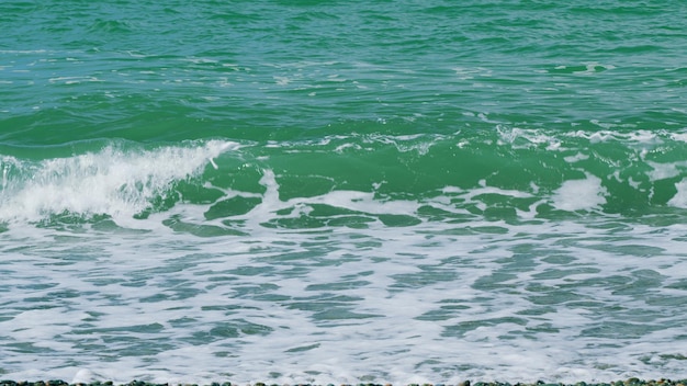 La superficie del mar la orilla del mar turquesa las olas del océano chocando contra la orilla y formando patrones de espuma en cámara lenta