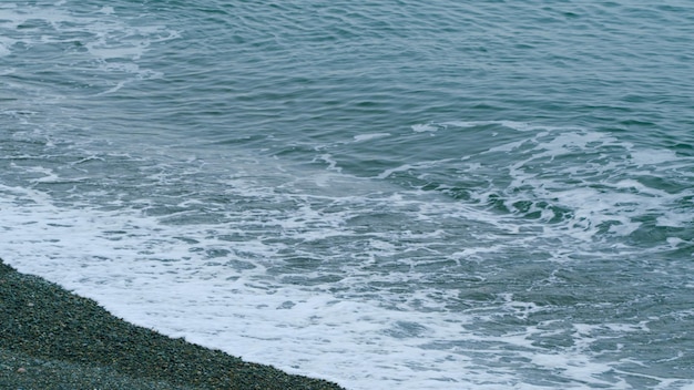 La superficie del mar tranquila borrosa las ondas espumosas suaves lavando la playa de guijarros todavía