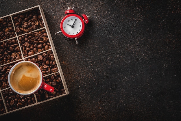 Superficie oscura con granos de café, un reloj despertador y una taza de café.