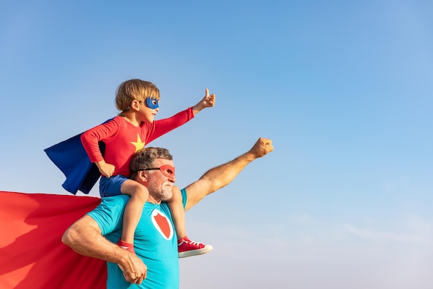 Superheld älterer Mann und Kind spielen im Freien. Großvater und Junge des Superhelden, die zusammen Spaß gegen Hintergrund des blauen Himmels haben. Familienurlaubskonzept. Alles gute zum Vatertag