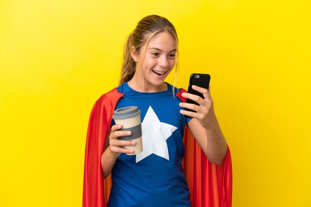 Superheld kleines Mädchen isoliert auf gelbem Hintergrund mit Kaffee zum Mitnehmen und einem Handy