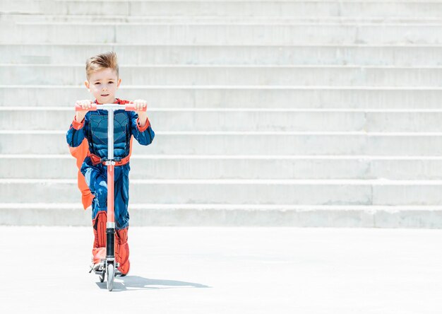 Superhelden-Kind mit Roller Junge, der Spaß im Freien hat Konzept der weiblichen Kraft und des Feminismus
