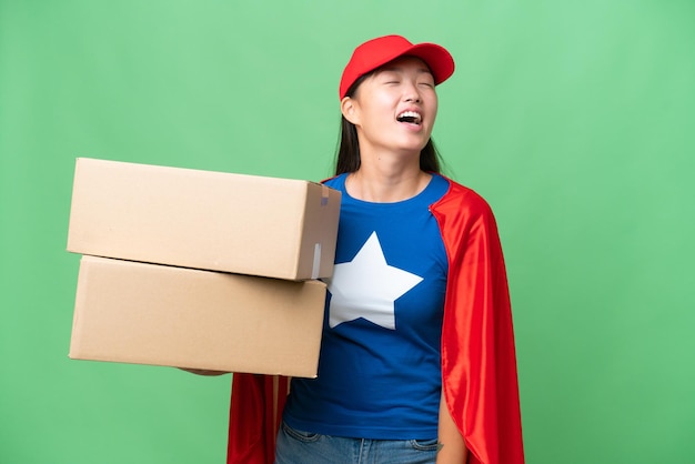 Superhelden-Lieferung Asiatische Frau, die Kisten über isoliertem Hintergrund hält, lacht