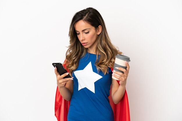 Superheldenfrau über isoliertem weißem Hintergrund mit Kaffee zum Mitnehmen und einem Handy