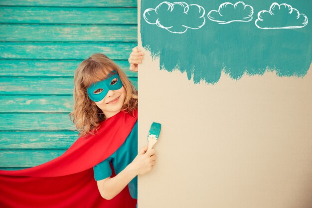 Superheldenkind, das die Wand mit blauer Farbe malt. Kind hat Spaß zu Hause. Frühjahrssanierungskonzept