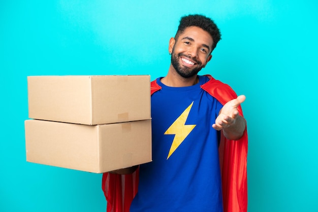 Superhéroe entrega hombre brasileño aislado sobre fondo azul estrechando la mano para cerrar un buen trato