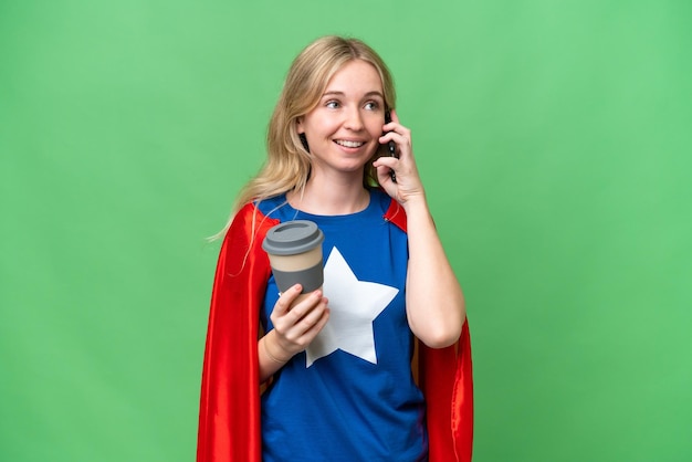 Foto superhéroe mujer inglesa sobre un fondo aislado sosteniendo café para llevar y un móvil