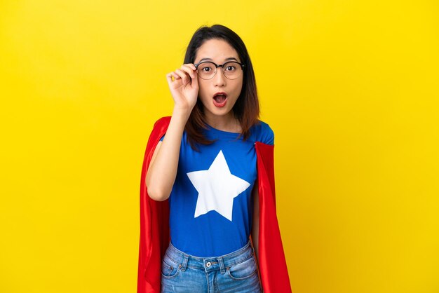 Superhéroe mujer vietnamita aislada de fondo amarillo con gafas y sorprendida