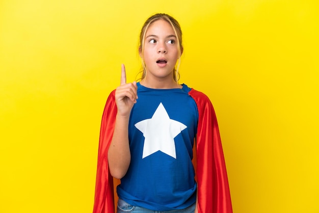 Foto superhéroe niña aislada sobre fondo amarillo pensando en una idea apuntando con el dedo hacia arriba