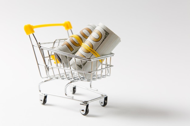 Supermarkt Lebensmittelgeschäft Push Cart zum Einkaufen mit gelben Elementen am Griff mit Bündeln von Dollar-Geld-Banknoten-Bargeld isoliert auf weißem Hintergrund. Konzept des Einkaufens. Kopieren Sie Platz für Werbung.