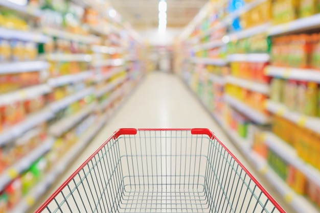 Supermarktgang mit leerem Einkaufswagen und Produktregalen innen defokussiert