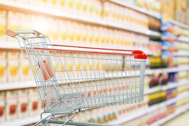 Supermercado com prateleiras de produtos de suco de frutas interior desfocar o fundo com carrinho de compras vazio