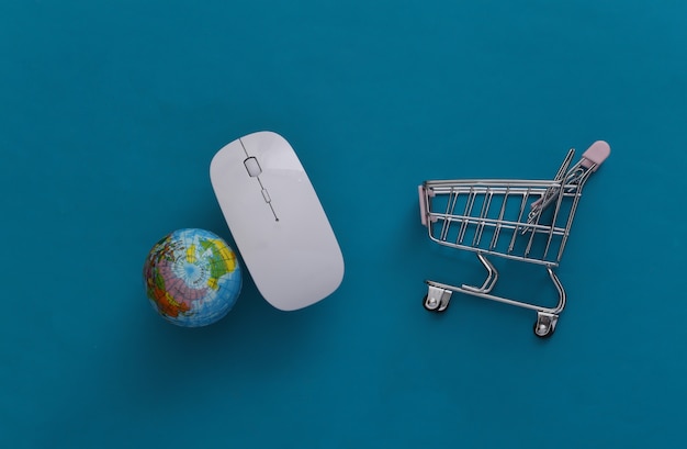 Supermercado global online. mouse do pc e mini carrinho de compras com globo sobre fundo azul. vista do topo. postura plana