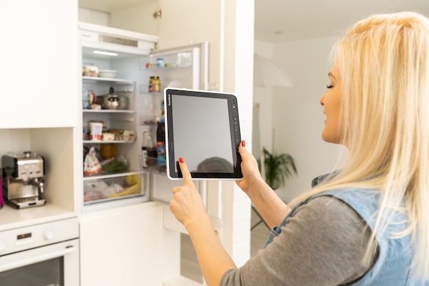 Foto supermercado en línea compras manos con icono de carrito de compras de tableta de computadora frente al refrigerador.