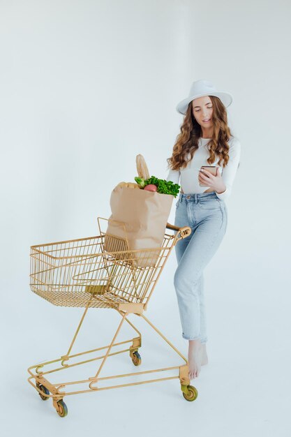 En el supermercado, la mujer usa un teléfono inteligente, se apoya en el carrito de la compra.