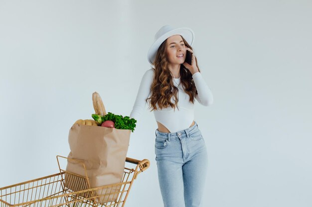 En el supermercado, la mujer usa un teléfono inteligente, se apoya en el carrito de la compra.