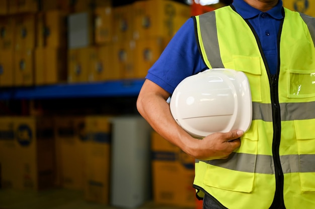 Foto supervisor de almacén masculino asiático recortado o trabajador en uniforme sosteniendo un casco blanco