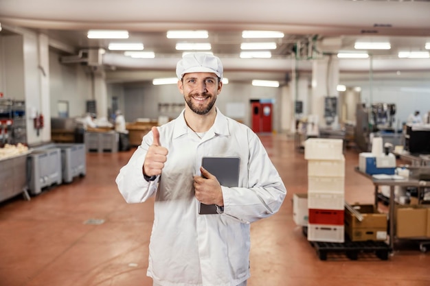 Un supervisor de la industria cárnica sostiene una tableta y da el visto bueno a la calidad de los productos.