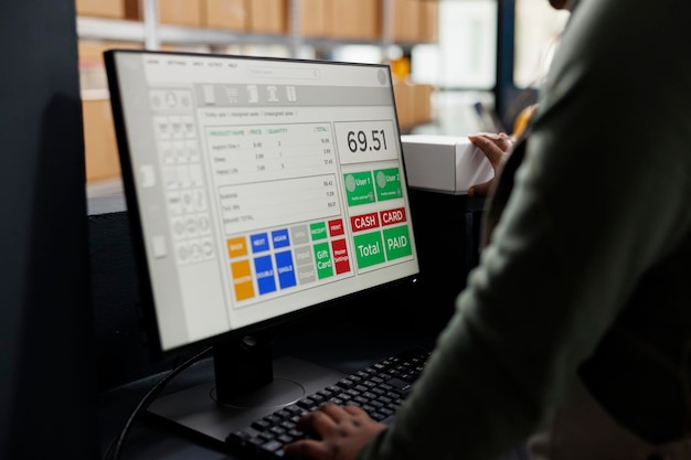 Supervisor mirando los detalles de envío de productos en la computadora, trabajando en los pedidos de los clientes preparando paquetes en el mostrador del almacén. Empleado afroamericano analizando logística de mercancías.