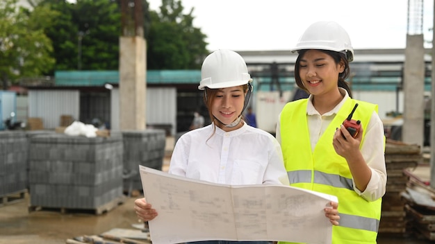 La supervisora asiática y el plan de control del arquitecto inspeccionan el sitio de construcción de edificios comerciales