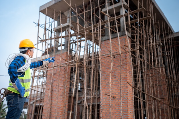 Supervisores ou contratados asiáticos estão assistindo a construção de grandes casas ou locais de trabalho em andamento.