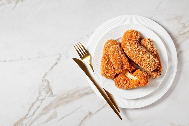 Suplemento italiano al telefono o croquetas de arroz rellenas de mozzarella servidas en un plato blanco con cubiertos dorados sobre un fondo de mármol claro, vista superior, espacio de copia