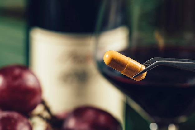 Foto suplementos de resveratrol com uvas borradas e um copo de vinho tinto no fundo