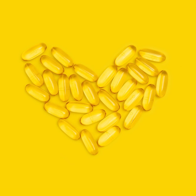 Suplementos nutricionais de cápsulas Omega3 em forma de coração na vista superior de fundo amarelo