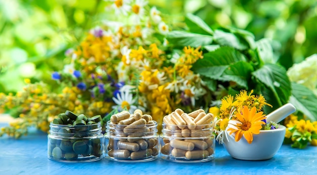 Suplementos, vitaminas y hierbas medicinales en frascos de vidrio sobre mesa azul con fondo de plantas borrosa