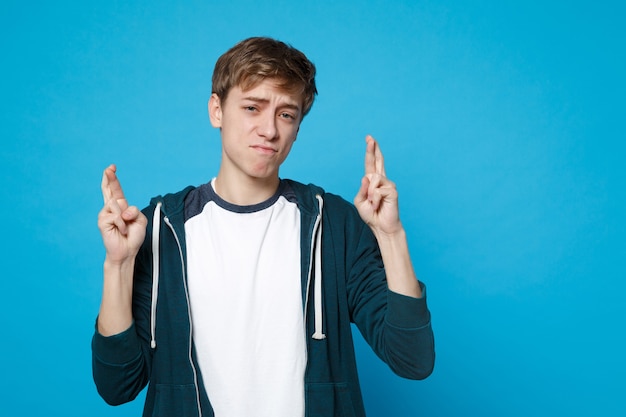 Suplicando a un joven en ropa casual esperando un momento especial, manteniendo los dedos cruzados, pidiendo deseo aislado