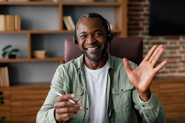 Foto suporte ao cliente e trabalho em casa gerente de cara afro-americano adulto sorridente em mãos casuais e de fones de ouvido
