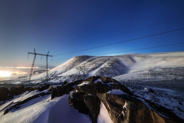 Suporte da linha de alta tensão Uma paisagem de montanha de noite de inverno