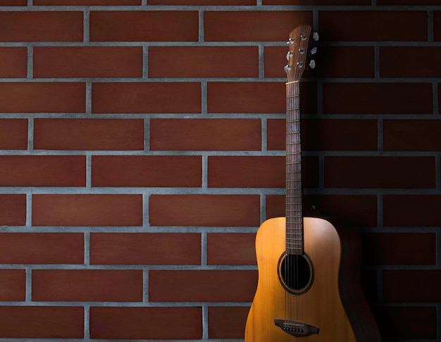 Suporte de guitarra acústica marrom na frente do fundo da parede de tijolos Parte do corpo da guitarra frontal feita com lado sólido superior e madeira de mogno traseira