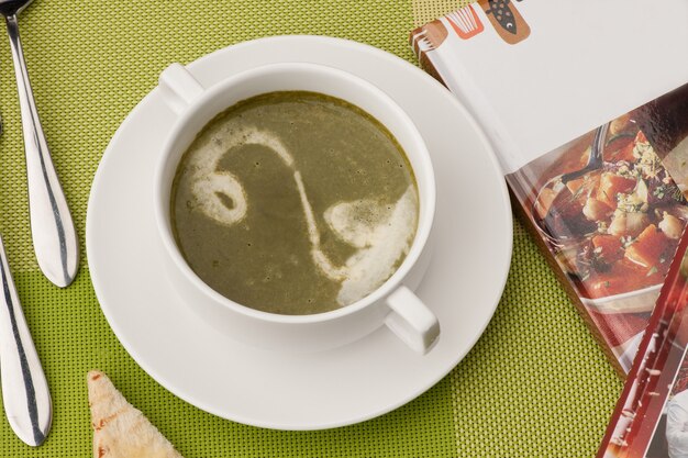 Suppe in einer weißen Schüssel mit Buch und Besteck auf einer grünen Tischdecke