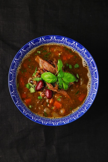 Suppe mit Bohnen und Fleisch in Schüssel auf dunkler Tischplattenansicht