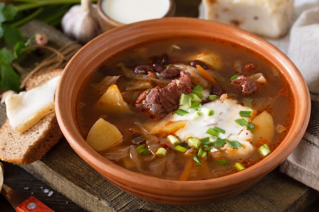 Suppe mit Fleisch und Bohnen oder Borschtsch-Nahaufnahme, serviert mit Sauerrahm auf einem rustikalen Holztisch