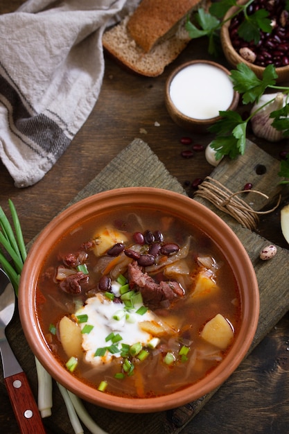 Foto suppe mit fleisch und bohnen oder borschtsch serviert mit sauerrahm auf einem rustikalen holztisch