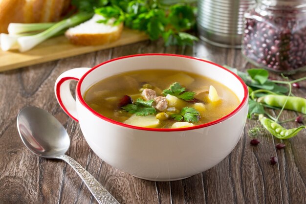 Suppe mit Fleisch und frischem Gemüse auf einem Holztisch