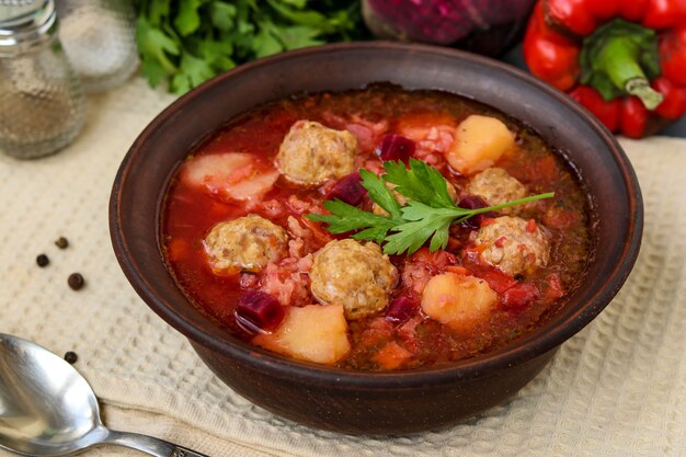 Suppe mit Fleischbällchen und Gemüse in einer dunklen Schüssel