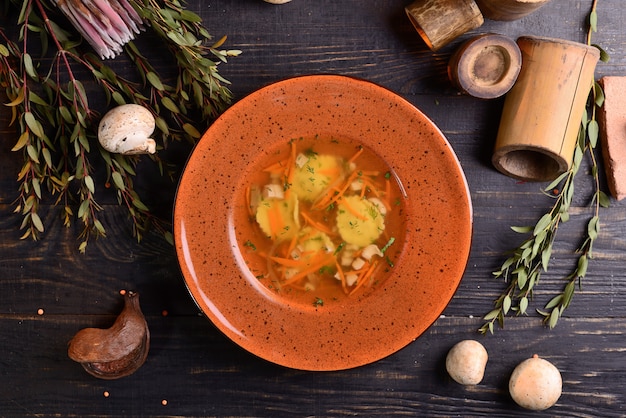 Suppe mit Pilzen und Karotten. auf einem schwarzen Holztisch mit Dekor