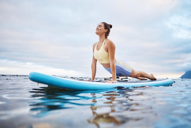 Surf no oceano e mulher fazendo ioga na prancha de manhã pronta para surfar e relaxar Esportes aquáticos de bem-estar e garota fazendo exercícios de alongamento no remo no mar desfrutam de ondas calmas e paz na natureza