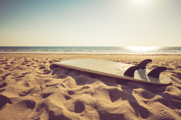 Surfbrett auf tropischem Strand des Sandes mit ruhigem See- und Sonnenunterganghintergrund des Meerblicks.