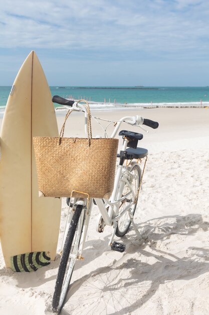 Surfbrettstrohtasche und Fahrrad am weißen Sandstrand gegen Seesport- und Erholungskonzept